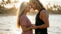 Two young blonde women sharing intimate moment during golden hour sunset by water, romantic couple embracing with warm backlighting and soft bokeh background.