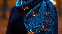 Glowing blue knitted scarf with sparkling lights and bokeh effect against dark background creates magical winter holiday atmosphere, suitable for seasonal designs.