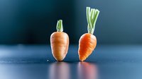 Fresh organic carrots with green tops floating against dark background with reflection, minimalist food photography composition for healthy eating concept.