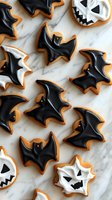 Halloween bat and ghost cookies with black and white icing on marble surface for spooky seasonal baking and party treats.