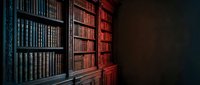 Vintage library interior with antique wooden bookshelves filled with old leather-bound books in warm atmospheric lighting for academic and literary projects.