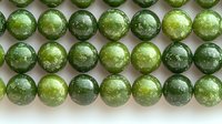 Rows of polished green jade beads showing natural stone patterns and textures against neutral background. Jewelry making supplies and gemstone elements.