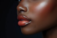 Close-up profile of young African American woman with glossy coral lips and flawless skin against dark background for beauty and cosmetics advertising.