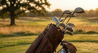 Golf bag with clubs on course during golden hour sunset creating warm atmospheric lighting for sports and recreation activities.