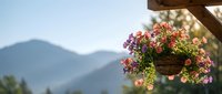 Colorful hanging flower basket with petunias and geraniums on wooden beam against mountain landscape background for garden and outdoor decoration concepts.