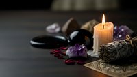 Mystical altar setup with burning candle, amethyst crystals, sage bundle and ritual tools for spiritual practices, meditation and energy healing ceremonies.