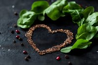 Heart shape made from scattered quinoa seeds on dark stone background with fresh green spinach leaves and pomegranate seeds, romantic healthy food concept.