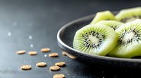 Fresh sliced kiwi fruit on black ceramic plate with vitamin supplements scattered on dark background, healthy eating and nutritional concept.