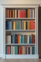 Classic white wooden bookshelf with colorful hardcover books arranged on four shelves against gray wall, featuring vintage volumes in red, blue, green and brown spines.