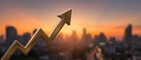 Golden arrow trending upward over blurred city skyline at sunset representing business growth, success, financial progress and economic development.