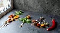 Colorful spices and herbs arranged on dark slate surface near window with natural lighting for culinary cooking and seasoning recipes.