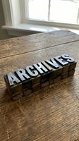 Vintage wooden letterpress blocks spelling ARCHIVES on rustic wood table near window for typography design projects and historical documentation concepts.