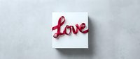 White gift box with red ribbon shaped into the word Love on a gray concrete background, perfect for Valentine's Day and romance.
