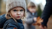 Young blonde girl with blue eyes wearing knit beanie and sweater looking at camera with serious expression during autumn outdoor family gathering.