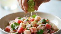 Hands squeezing fresh lime juice over colorful ceviche with diced fish, tomatoes, cilantro and onions in white bowl for seafood cooking and recipe preparation.