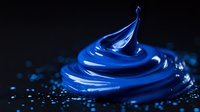 Vibrant blue paint swirl with glossy texture and droplets on dark background creates dynamic motion effect for artistic and design projects.