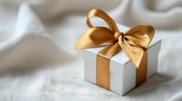 White gift box with elegant gold ribbon bow on soft fabric background for special occasions and celebrations.
