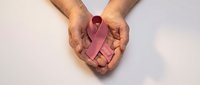 Hands gently holding pink awareness ribbon symbol for breast cancer support and healthcare advocacy on clean white background.