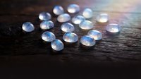 Sparkling crystal gemstones scattered on dark wooden surface with rainbow light reflections creating magical prismatic effects for jewelry design.