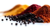 Colorful spice powders and black peppercorns arranged on white surface for culinary cooking and seasoning applications in kitchen food preparation.