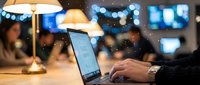 Young Caucasian male professional typing on laptop in cozy office with bokeh lights, warm lamp glow, and colleagues in background.