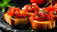 Fresh tomato bruschetta with herbs on toasted bread slices, served on dark stone background. Traditional Italian appetizer for restaurant menu.