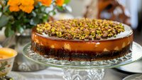 Decadent chocolate cheesecake with caramel glaze and pistachio topping on glass cake stand, perfect for bakery, dessert, and food photography projects.