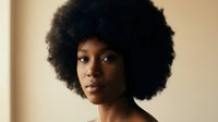 Young African American woman with natural afro hairstyle looking confidently at camera in warm indoor lighting for beauty and lifestyle concepts.