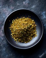 Dried aromatic herbs and spices mixture in black ceramic bowl on dark textured background, overhead view for culinary and food photography.