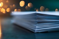 Stack of white paper sheets with blurred golden bokeh lights in background on dark surface, creating atmospheric business or educational setting.