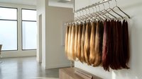 Professional hair extension display rack showcasing various brown and blonde human hair pieces in modern salon interior with natural lighting.