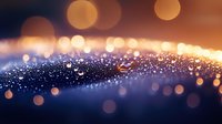 Glowing golden bokeh lights and sparkles on dark blue background create magical atmospheric effect with soft focus and depth for festive designs.