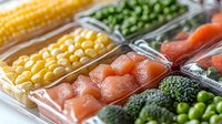 Fresh raw ingredients in plastic containers including salmon cubes, corn, peas, broccoli and carrots arranged in rows, ready for meal preparation and cooking.