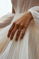 Elegant female hand with engagement ring gently touching flowing white fabric, creating soft pleats and folds against warm skin tone. Perfect for wedding photography.