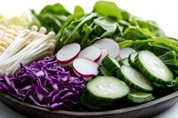 Fresh sliced vegetables and enoki mushrooms on dark plate including purple cabbage, cucumber, radish and spinach leaves arranged for Asian cuisine.