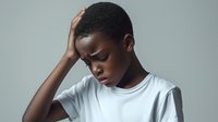 Young African American man experiencing headache holding head with hand showing stress fatigue or mental health struggle on gray background.