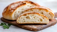 Freshly baked artisan bread with crispy crust and airy crumb texture, sliced to show interior structure, served on wooden cutting board.