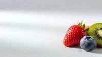 Fresh mixed berries and kiwi slice on white surface with copy space for healthy eating and nutrition concepts.