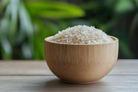 Raw white jasmine rice grains in bamboo bowl on wooden table against blurred green natural background, healthy Asian cuisine ingredient.