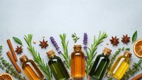Essential oils in glass bottles with fresh herbs, spices and dried citrus on white background for aromatherapy and natural wellness products.