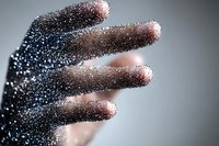 Glittering particles covering human fingers create magical sparkle effect against blurred background, dramatic lighting enhances mysterious atmosphere.