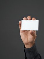 Male hand holding blank white business card against gray background, ideal for corporate branding and professional networking designs.