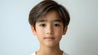 Young Asian boy with stylish brown hair and blue eyes against neutral background, showcasing natural beauty and innocence for portrait photography.