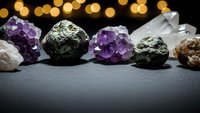 Collection of healing crystals and gemstones including amethyst, pyrite, and quartz arranged on dark surface with warm bokeh lights for spiritual wellness.