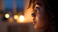 Young African American woman in profile view illuminated by warm evening light with bokeh background, expressing thoughtful contemplation and serenity.