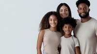 Happy African American family of four wearing matching beige outfits posing together against white background for portrait photography and lifestyle content.