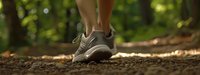 Close-up of athletic shoes on forest trail path with sunlight filtering through trees, showcasing outdoor fitness and nature walking adventure.
