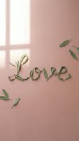 Word Love made of green leaves on a soft pink background with gentle sunlight shadows, romantic nature lettering for cards.