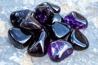 Polished purple and black gemstones scattered on textured surface for jewelry making, crystal healing, meditation and spiritual wellness practices.