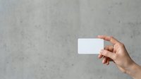 Woman's hand holding blank white business card against textured gray concrete wall background for corporate branding and marketing mockup presentations.